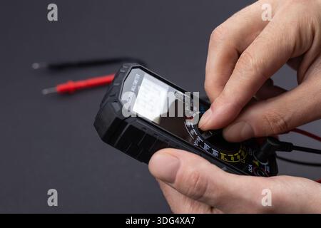 Cropped image of male repairman checking fridge with digital multimeter at home. Stock Photo