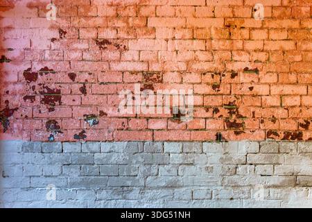 Old crumbling red brick wall half painted white. Abstract vintage background. Stock Photo