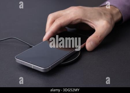 Man Charging Smartphone Using Wireless Charging Pad At Home. Stock Photo