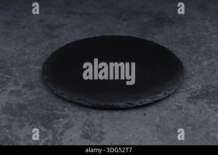 Round rustic black slate stone plate, on stone background. Stock Photo
