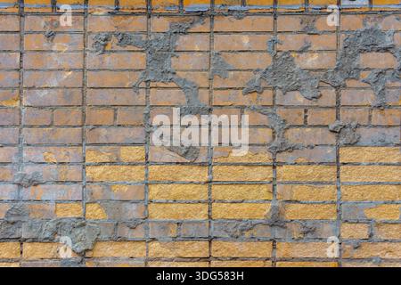 A yellow brick wall is marked with irregular splashes of cement. The rough contrast adds an unfinished, industrial character. Stock Photo