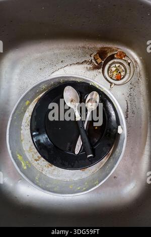A close-up shot of an unsanitary kitchen sink filled with dirty dishes, spoons, and leftover food, ideal for themes of domestic life and hygiene. Stock Photo