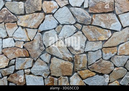 Natural stone wall with irregular rock pattern, ideal as an architectural or rustic background Stock Photo