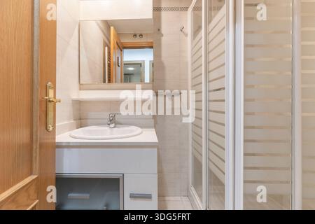 An earthy color palette creates a serene atmosphere, with rectangular beige tiles arranged in a herringbone pattern, teak wood in the vanity, and touc Stock Photo