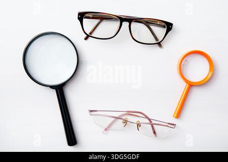 Frame made from various vision-enhancing tools—glasses and magnifying lenses—top view, white background. Stock Photo