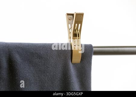 A close-up shows dark blue fabric, possibly garment, secured by a large, tan plastic clothespin on a metal rod. The stark white background emphasizes Stock Photo