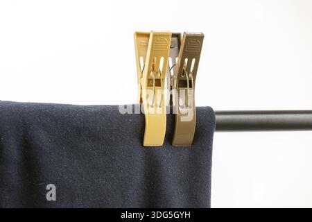 Two plastic clothespins, two beige and one brown, firmly secure a dark blue fabric onto a metal rod, symbolizing everyday laundry on a practical cloth Stock Photo
