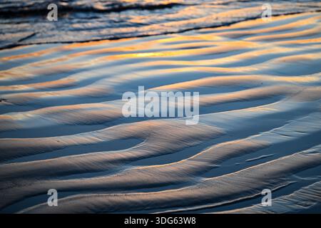 Ripples in wet sand reflect the soft glow of a sunset over the ocean waves. Tofino, British Columbia, Canada Stock Photo
