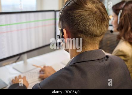 Male call center agent at dual monitors using headset in modern office workspace Stock Photo