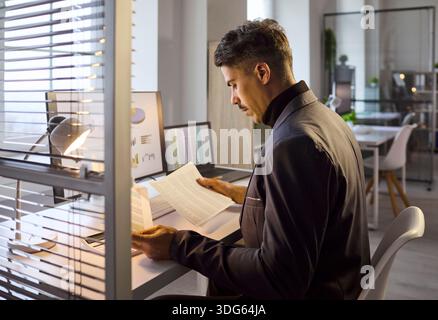 Businessman analyzing printed reports by laptop with graphs on screen in office Stock Photo