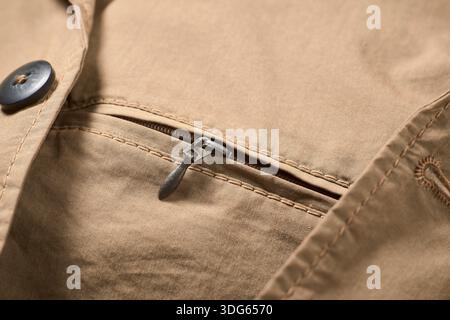 Close-up of a tan fabric zipper on a stitched pocket with a black button nearby. Stock Photo