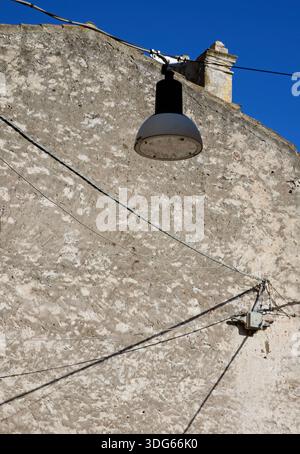 A streetlight hangs from a wire against the grey wall of an old house, Sardinia, Italy Stock Photo