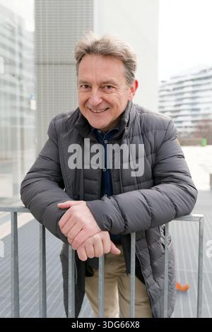 Mature man in a puffer jacket leaning on a metal railing outdoors, urban background. Italy Stock Photo