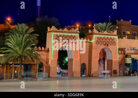 Brightly lit historic gate with neon lights framed by palm trees at night under deep blue sky. Ouarzazate, Morocco Stock Photo
