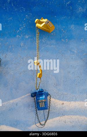 Yellow and blue vintage telephones on a textured, painted blue wall. Ouarzazate, Morocco Stock Photo