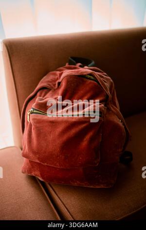 Soft red backpack on a brown sofa under warm sunlight. Chengdu, Sichuan, China Stock Photo