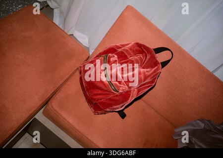 Red velvet backpack on an orange sofa with a curtain backdrop. Chengdu, Sichuan, China Stock Photo