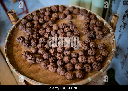 A woven basket filled with whole walnuts on a wooden surface. Chengdu, Sichuan, China Stock Photo
