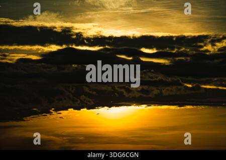 Dramatic sunrise with intense golden sunlight breaking through dark heavy silhouettes of clouds in the morning sky. Stock Photo