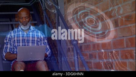 Sitting senior man using laptop on metal stairs, wearing plaid shirt and shorts, HUD overlay Stock Photo