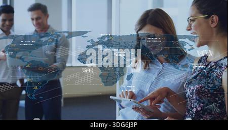Pointing two women in casual attire examining tablet in office, digital map, men viewing handheld Stock Photo