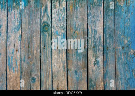 Wooden surface made of vertical planks with uneven coating. Old blue paint is partially worn off, revealing wood with brown-gray tones. Stock Photo