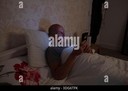 Middle aged man with micro habits which form part of his daily routine including checking emails on a smartphone before bedtime. Stock Photo