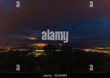 A dramatic thunderstorm illuminates the sprawling cityscape of Seetal valley below, with a vibrant flash of lightning striking across the horizon and Stock Photo