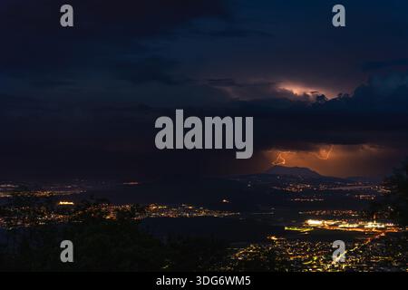 A dramatic thunderstorm illuminates the town and surrounding mountains below, showcasing the Rigi region of Switzerland with a striking flash of light Stock Photo