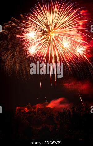 A spectacular display of vibrant fireworks explodes above Schloss Lenzburg, casting a warm glow upon the historic castle silhouetted against a dark ni Stock Photo