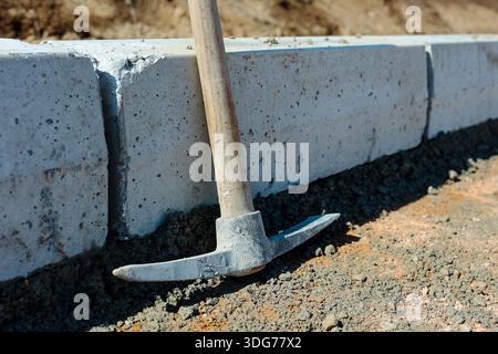 Pickaxe Leaning Against Concrete Curb at Construction Site Stock Photo