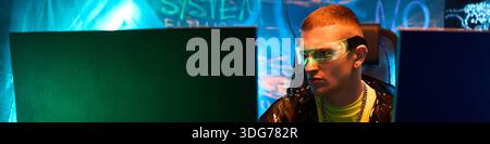 Header of young adult Caucasian man, wearing futuristic glasses, sitting at desk working on computer monitors in dark room, with neon blue lighting and digital graffiti on walls Stock Photo