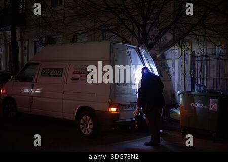 Kyiv, Ukraine – Dec 21, 2022: A delivery worker uses a bright flashlight on a dark, snow-covered Lysenka Street. Total power outage in the historic ce Stock Photo