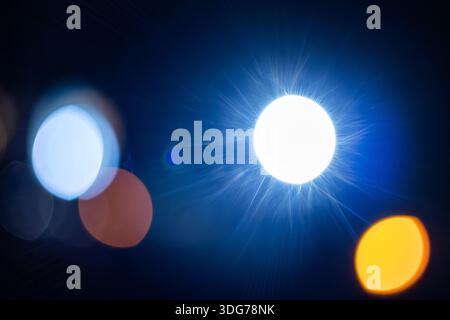 Bright blue light source with lens flare and soft orange bokeh circles on a black background. Minimalist abstract composition of urban night lights in Stock Photo