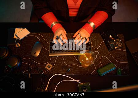 Unrecognizable young woman typing on keyboard surrounded by computer hardware, external hard drive, circuit board, mouse, headphones, and various electronic components Stock Photo