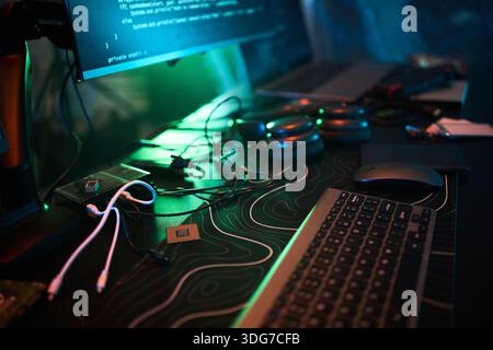 Closeup showing computer keyboard, mouse, circuit boards, headphones, and monitor displaying code, illustrating hacker workspace with electronic components and tangled cables Stock Photo