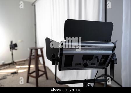 Photo studio setup with lighting equipment and chair. Professional interior for photography with white backdrop and LED panel with barn doors for port Stock Photo