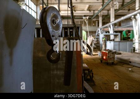 Close up of a heavy duty metal pulley with cable and hook in a vintage manufacturing hall. Industrial lifting equipment and mechanical engineering har Stock Photo