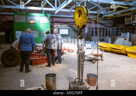 Group of mechanics working on heavy equipment in a large factory hall. Professional maintenance and repair process in industrial facility. Engineering Stock Photo