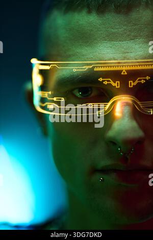Portrait of young adult Caucasian man wearing futuristic augmented reality glasses with digital interface, looking into camera, facial piercings visible, cyberpunk hacker concept Stock Photo