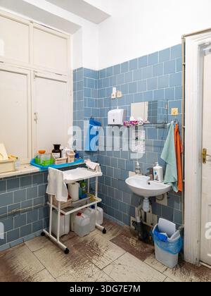Kyiv, Ukraine – Nov 11, 2025: Cluttered treatment room in a state hospital with old blue wall tiles and rusty plumbing. Poor sanitary conditions in a Stock Photo