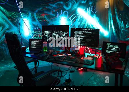 Empty workstation featuring multiple monitors displaying code and hacking tools, illuminated by neon lights with digital devices and accessories scattered across desk in dark room Stock Photo