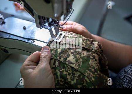 Industrial sewing machine making military uniform parts. Close up of professional tailoring process with tactical camouflage fabric and velcro element Stock Photo
