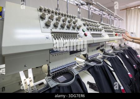 Close up of multi head embroidery machine in garment factory. High tech automated equipment for stitching logos on restaurant workwear and chef aprons Stock Photo