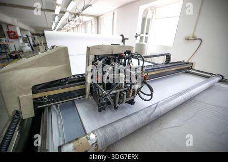 Industrial garment factory with CNC fabric cutting machine. High tech automated technology for high precision textile processing and mass production o Stock Photo