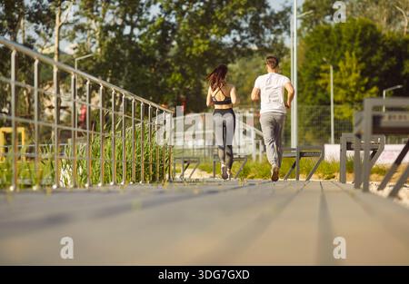 Couple running together on bright sunny day, jogging along outdoor path or bridge, focused active  Stock Photo