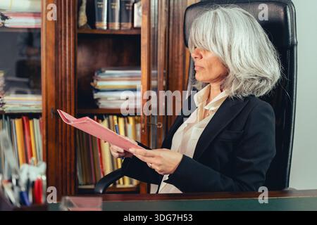 Senior businesswoman reading documents at her desk in a traditional office. Concept of decision making, responsibility, leadership and professional ex Stock Photo