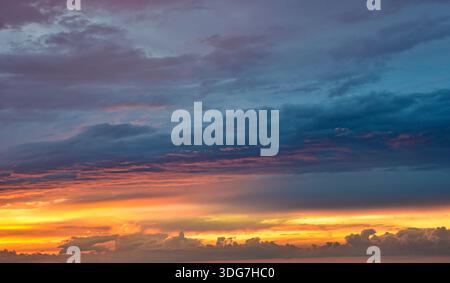 Intense contrast between a deep blue evening sky and vibrant, fiery orange clouds illuminated by the setting sun at dusk. Stock Photo