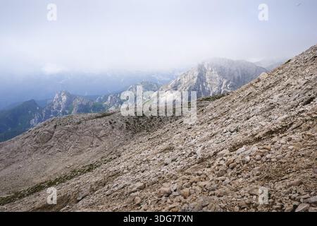 Stunning, misty view of Triglav mountain range with sharp mountain ridges under a cloudy sky Stock Photo