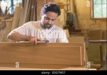 Young man carefully hand sanding wood in woodshop, New Jersey, USA Stock Photo